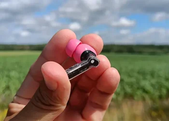 Anmelder holder en rosa Nothing Ear (3a)-høretelefon i sin hånd med mark i baggrunden