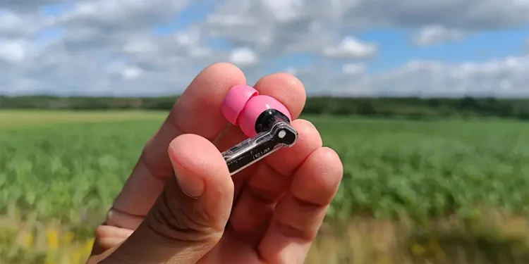 Anmelder holder en rosa Nothing Ear (3a)-høretelefon i sin hånd med mark i baggrunden