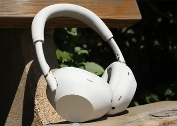 Platin- og sølvfarvede Sony WH-1000XM6 lænet mod ryglænet på en træbænk i solen