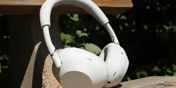 Platin- og sølvfarvede Sony WH-1000XM6 lænet mod ryglænet på en træbænk i solen