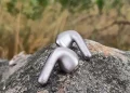 Et par Xiaomi Buds 6 Nebula Purple placeret på en stor sten med bølgende græs i baggrunden