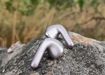 Et par Xiaomi Buds 6 Nebula Purple placeret på en stor sten med bølgende græs i baggrunden