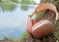 Apple AirPods Max 2 Orange lænet mod en træstamme med en å i baggrunden