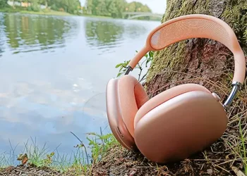 Apple AirPods Max 2 Orange lænet mod en træstamme med en å i baggrunden