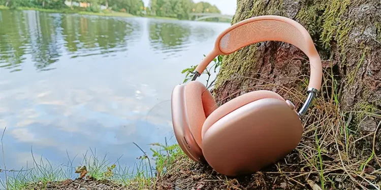 Apple AirPods Max 2 Orange lænet mod en træstamme med en å i baggrunden