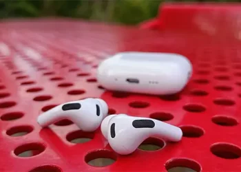 Apple AirPods Pro 3 liggende på et perforeret rødt bord i stål med opladningsetuiet bagved