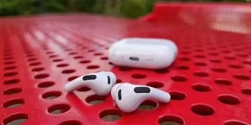 Apple AirPods Pro 3 liggende på et perforeret rødt bord i stål med opladningsetuiet bagved