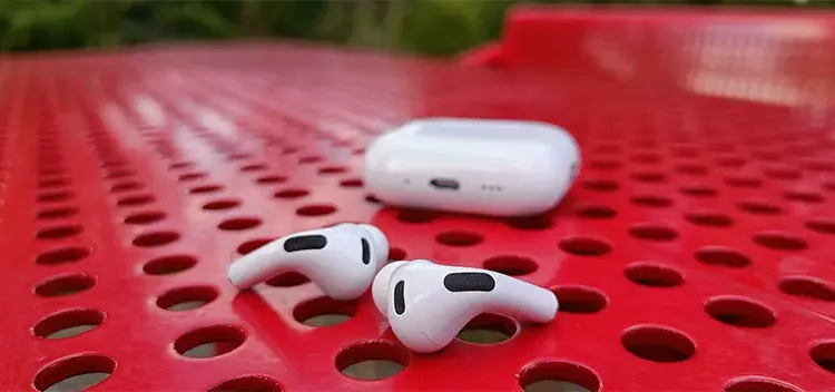 Apple AirPods Pro 3 liggende på et perforeret rødt bord i stål med opladningsetuiet bagved