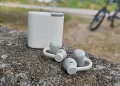 Lysegrå CMF Clip Pro med opladningsetuiet i baggrunden på en grå betonbarriere