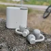 Lysegrå CMF Clip Pro med opladningsetuiet i baggrunden på en grå betonbarriere